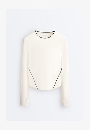 Dlhý rukáv, biely top s čiernym lemovaním na golieri a stranách, s otvorom na palec v manžetách a mierne zaobleným spodným okrajom.