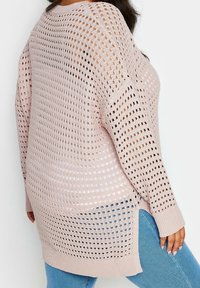 Pull en tricot surdimensionné rose clair, avec un tissage lâche et des grands trous, des manches longues et des poignets côtelés, associé à un jean bleu.