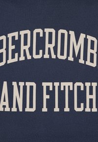 Μπλε ναυτικού υφάσματος με έντονο, λευκό κείμενο που γράφει "ABERCROMBIE AND FITCH", παρουσιασμένο σε μεγάλη, αποκλειστική γραμματοσειρά με υφή.