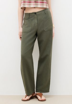 Kvinde iført olivengrønne bukser med vide ben og frontlommer, kombineret med brune flade sandaler og en cropped ternet skjorte.