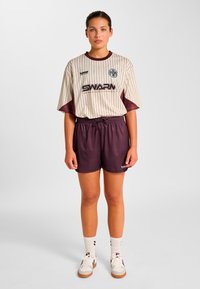 Kortärmad randig tröja i gräddvit och mörkröd med "SWARM"-logotyp, kombinerad med mörkröda shorts. Skorna är vita med mörkröda detaljer och beige sulor.