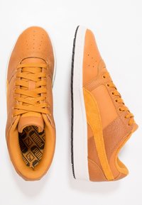 Baskets en cuir marron avec des accents texturés, bout perforé, semelles blanches et noires, et un intérieur à motif géométrique.