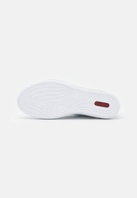 Semelle de chaussure avec un design en caoutchouc blanc, texturée pour une meilleure adhérence, mettant en avant un motif de vagues subtil et un logo "Rieker" bordeaux.