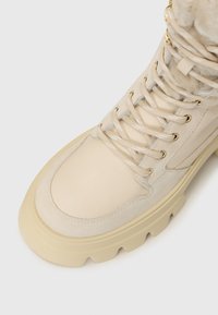 Krémszínű bőr és velúr bokapuszta, kerek orral, vastag gumitalppal és fém fűzőlyukakkal, bolyhos műszőrme gallérral.