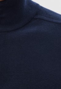 Mörkblå ribbad polotröja i tyg som täcker axlar och nacke, och visar en fin stickad struktur.