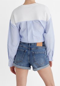 Camicia a righe blu e bianche oversize con maniche lunghe, abbinata a pantaloni corti di jeans con orlo arrotolato, dotati di tasche posteriori e un'etichetta in pelle.
