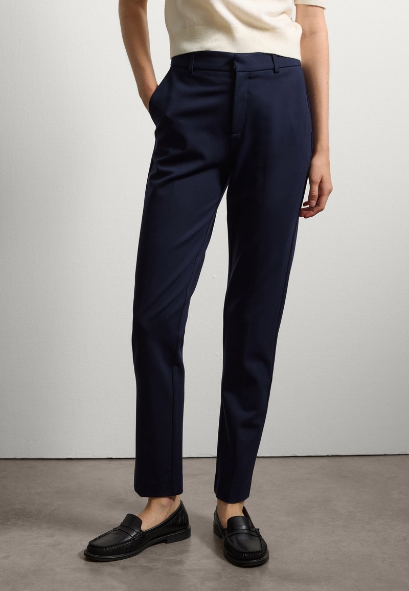 Pantaloni sartoriali blu scuro realizzati in tessuto morbido, con tasche laterali e un design slim fit. Abbinati a mocassini neri piatti.