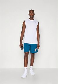 Valge varrukateta sportlik särk, türkiissinised lühikesed püksid valge logoga, hoiab käes musta veepudelit, kannab valgeid tossusid.