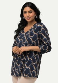 Mörkblå V-ringad topp med ett geometriskt mönster i beige och ljusblått. Mjuk tyg, trekvartslånga ärmar och avslappnad passform.