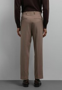 Pantalon habillé kaki à coupe droite, doté de deux poches arrière et d'une texture lisse. Associé à des chaussures marron foncé, sur un fond gris.