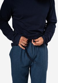 Donkerblauwe langemouwen shirt met aangesloten mouwen; blauwe geblokte pyjamabroek met een elastische tailleband en trekkoord.