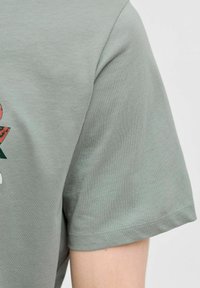 Lysegrøn bomulds T-shirt med korte ærmer, prydet med et tekstureret grafisk print på forsiden og en lige nederkant.
