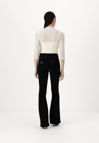 Top de encaje con mangas tres cuartos y dobladillo con puntilla, combinado con jeans negros ajustados y acampanados. Presenta una cintura sin costuras con bolsillos traseros.
