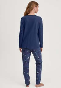 Marineblauw lange mouwen top, gecombineerd met een pantalon met een patroon van hemelse ontwerpen in donkere tinten, ananassen, sterren en felle accenten.