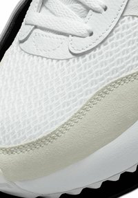 Scarpa sportiva bianca con una tomaia in mesh traspirante, dettagli in pelle liscia, suola texturizzata e una sottile striscia color crema lungo il bordo.