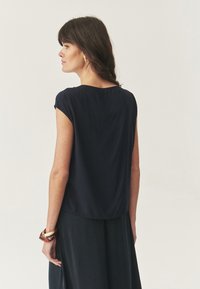 Top blu navy a maniche corte in tessuto morbido, caratterizzato da una vestibilità comoda e un scollo rotondo, abbinato a una gonna nera con texture.