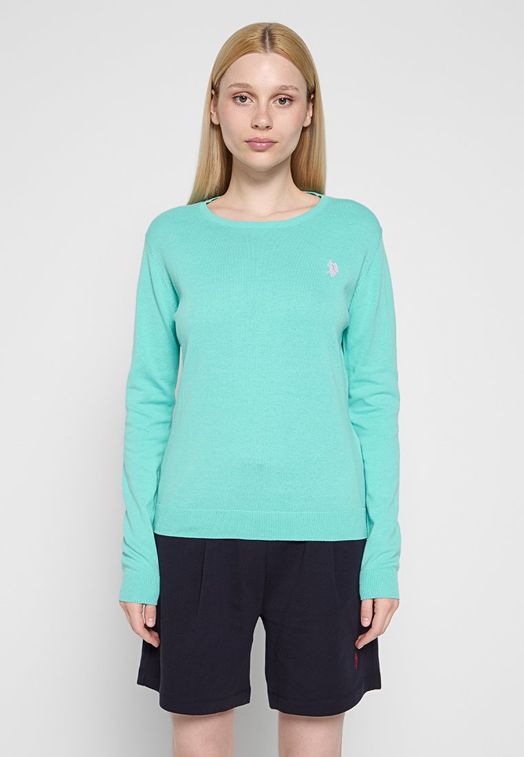 Helles teal Strickoberteil mit langen Ärmeln und rundem Ausschnitt; verfügt über ein kleines gesticktes Logo auf der Brust und einen gerippten Saum.