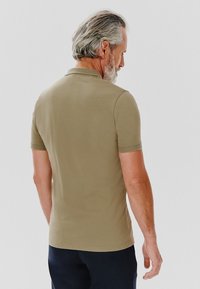 Koszulka polo z krótkim rękawem w jasnej oliwkowej zieleni, z prostym kołnierzykiem i gładkim, teksturowanym materiałem, widziana z tyłu.