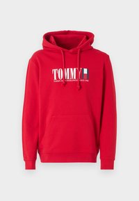 Felpa rossa in cotone con cappuccio regolabile. Include una tasca frontale e un logo stampato bianco con testo e un piccolo dettaglio della bandiera francese.