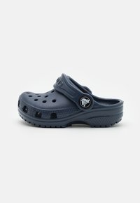 Navy blue clogs made of lightweight plastic, featuring ventilation holes, a back strap, and a logo badge on the side. Rubber sole for grip.