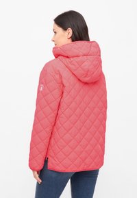 Chaqueta acolchada rosa con capucha, que presenta acabados en contraste, bolsillos laterales y un parche con el logotipo en la manga. Tejido suave y ligero.