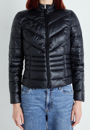 Black padded jacket with a zip closure, featuring a chevron pattern, ribbed texture, and long sleeves. Worn over blue denim jeans.