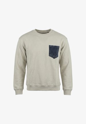 Felpa beige a maniche lunghe con polsini e orlo a costine, caratterizzata da una tasca sul petto in denim blu scuro sul lato sinistro.