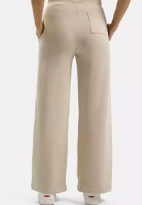 Beżowe spodnie o szerokich nogawkach, wykonane z miękkiego materiału, z tylną kieszenią i elastycznym pasem. Połączone z białymi trampkami z czerwonymi akcentami.