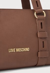 Ruda odinė rankinė su auksiniu "LOVE MOSCHINO" logotipu ir reguliuojama dirželiu su aukso žiedų aksesuarais.