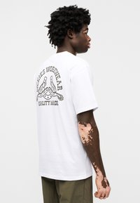 Λευκό βαμβακερό T-shirt με τυπωμένο σχέδιο που περιλαμβάνει το "Dickies Workwear" και ένα γραφικό πέταλο στην πίσω πλευρά. Λαιμός με ρίγα, κοντά μανίκια.