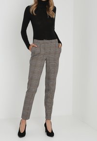 Szare spodnie w kratę o dopasowanym kroju, z bocznymi kieszeniami i gładką teksturą, w połączeniu z czarnym swetrem z długim rękawem i kołnierzem.