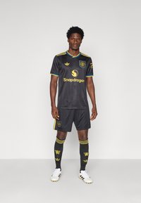 Μαύρη ποδοσφαιρική στολή με κίτρινες λεπτομέρειες. Διαθέτει κοντά μανίκια, κολλητό λαιμόκομμα, λογότυπο και χορηγό. Περιλαμβάνει σορτς και κάλτσες έως το γόνατο.