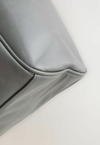Grijze leren handtas met een gladde textuur, hoekige vorm en zichtbare stikseldetails langs de naad en de onderrand.