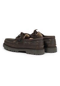 Zapatos de barco de cuero marrón con una superficie texturada, puntera redonda y suela de goma elevada. Presentan cordones y detalles de costura decorativa.