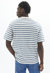Striped short-sleeve shirt in cream and light blue, featuring a relaxed fit and a round neckline. Smooth texture, casual design.