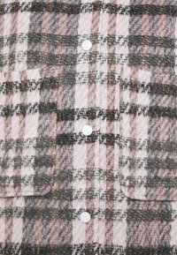 Geruite wollen shirt in roze, grijs en wit. Bevat grote opgestikte zakken en witte knopen. Zachte textuur met een warme, geweven uitstraling.