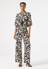 Schwarz- und cremefarbenes, blühendes Muster im Zweiteiler mit einer lässigen, kurzärmligen Bluse und weitem Hosenbein, das einen gebundenen Ausschnitt aufweist.