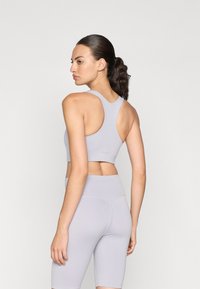 Sostenedor deportivo gris claro con diseño de espalda en forma de Y, combinado con shorts de tiro alto a juego, mostrando una tela suave y elástica y una silueta ajustada.