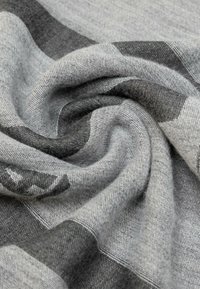 Tessuto a quadri grigio e carbone con una superficie morbida e texturizzata, drappeggiato per mostrare la sua sensazione soffice e i dettagli del motivo intrecciato.