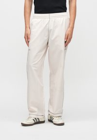 Ανοιχτό μπεζ, ελαφριά παντελόνια με ελαστική μέση και πλαϊνές τσέπες. Διαθέτουν αντίθετη γκρι ραφή και λεπτή, ίσια γραμμή ποδιού.