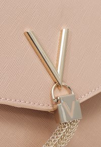 Light pink textured handbag flap with gold V-shaped metal clasp and small lock detail attached to fine gold chains.