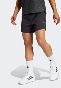 Pantalones cortos deportivos negros con un diseño ligero, con aberturas laterales y un logotipo sutil. Se llevan con calcetines blancos y zapatillas blancas con detalles negros.