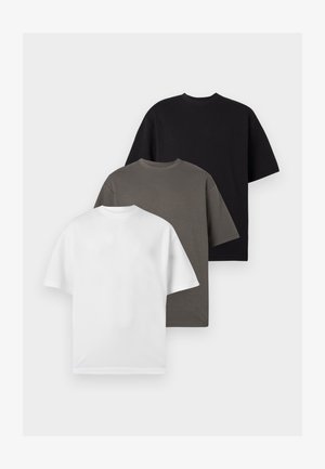 Drie effen T-shirts met korte mouwen en ronde hals opgestapeld, kleuren van voor naar achter: wit, grijs en zwart, op een lichtgrijze achtergrond.