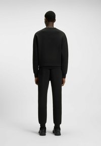 Black sweatshirt and pants set, made of smooth fabric, featuring a crew neck, ribbed cuffs, and a tapered leg design.