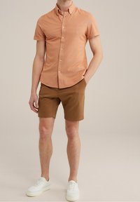 Svetle oranžová košile s krátkým rukávem a límečkem, spárovaná s hnědými šortkami a bílými teniskami. Hladká textura a přiléhavý střih.