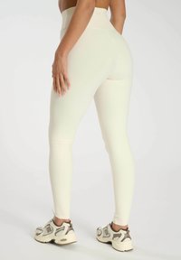 Leggings taille haute de couleur crème avec une texture côtelée, une forme ajustée et une finition lisse. Associés à des baskets de texture légère.