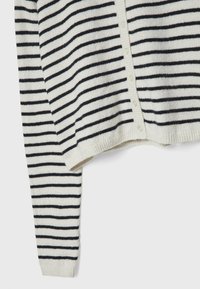 Cardigan blanc avec des rayures horizontales noires et de petits boutons sur le devant, montré partiellement avec une manche visible.