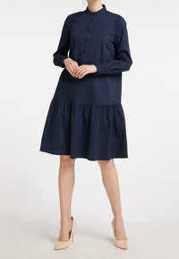 Abito blu navy con bottoni, colletto alla mandarino, maniche lunghe e gonna a strati svasata. Tessuto in cotone morbido con una vestibilità comoda.