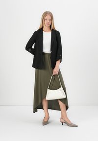 Zwarte blazer, witte top, olijfgroene rok en grijze hoge hakken. Witte handtas met decoratieve veters. Eenvoudig, gestructureerd ontwerp.