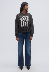 Σκούρο γκρι φούτερ με το κείμενο «LOVE YOUR LIFE» σε λευκό. Συνδυασμένο με τζιν φαρδιάς γραμμής σε μπλε και μαύρες μπότες μέχρι τον αστράγαλο. Μαλακό ύφασμα και άνετη εφαρμογή.
